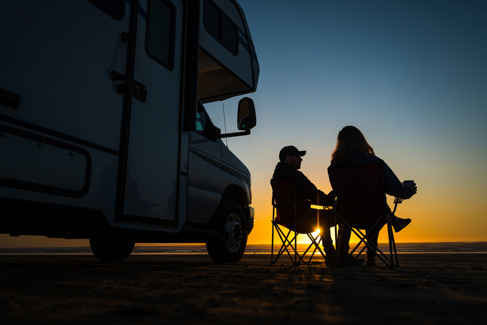 Caucasian Couple Relaxing Next to Their RV Motorhome on a Beach